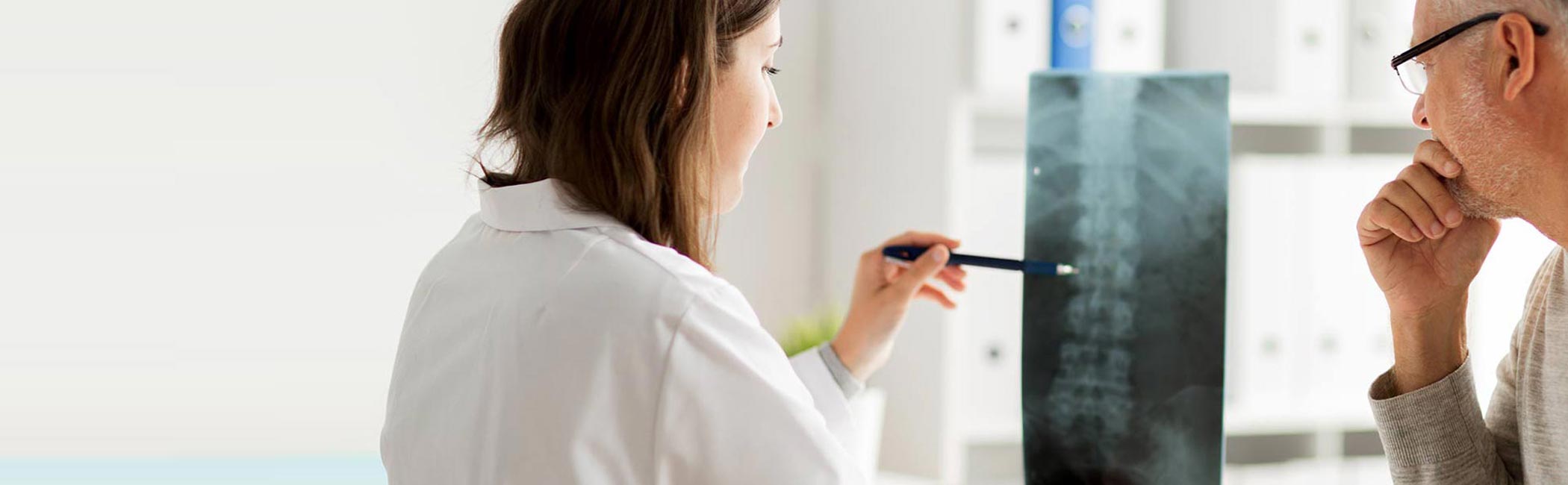 En læge sidder på et af Aleris hospitaler og kigger på et røntgenbillede af en rygsøjle.