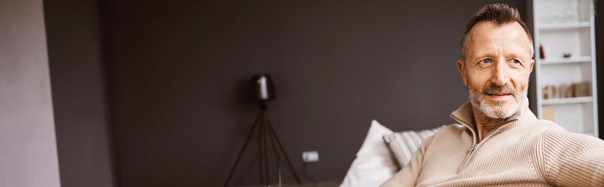 Smilende midaldrende mand sidder i sofa og kigger mod sin venstre side.