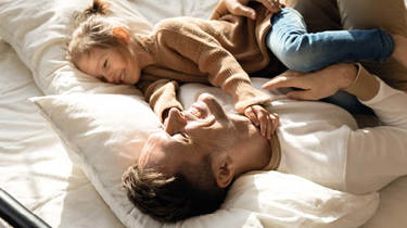 Far og datter ligger i sengen og griner.