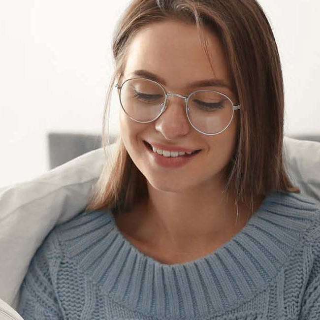 Glad ung kvinde sidder i en seng med dynen om sig. Hun kigger ned på noget.