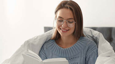 Glad ung kvinde sidder i en seng med dynen om sig. Hun kigger ned på noget.