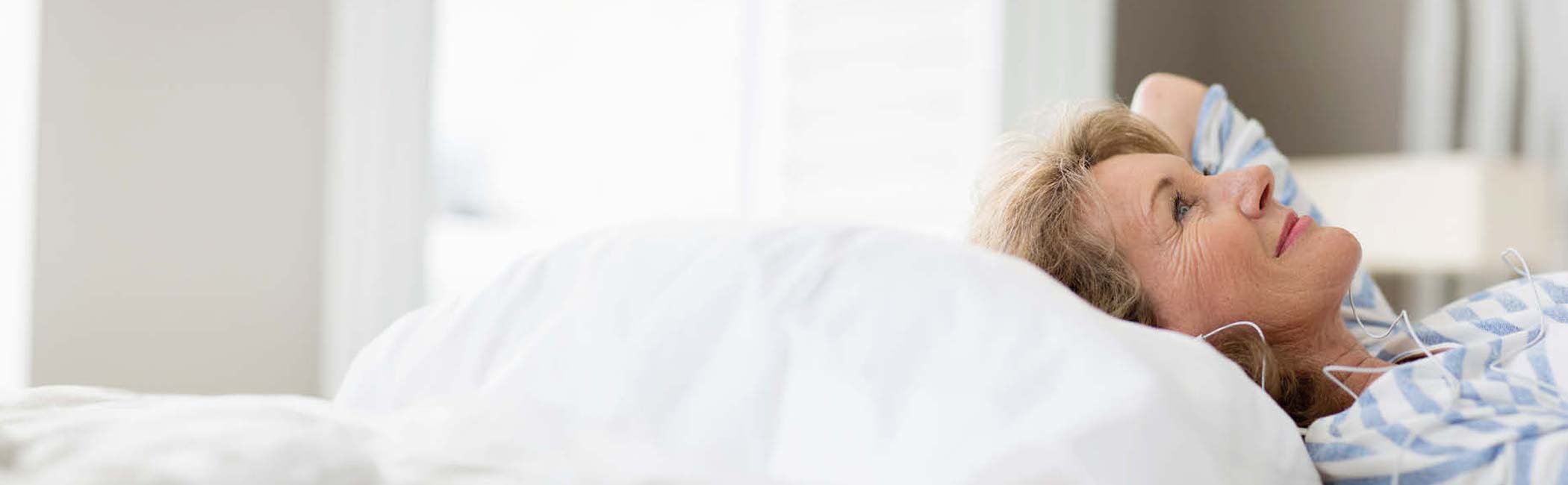 Glad kvinde ligger på ryggen i sengen med høretelefoner på.