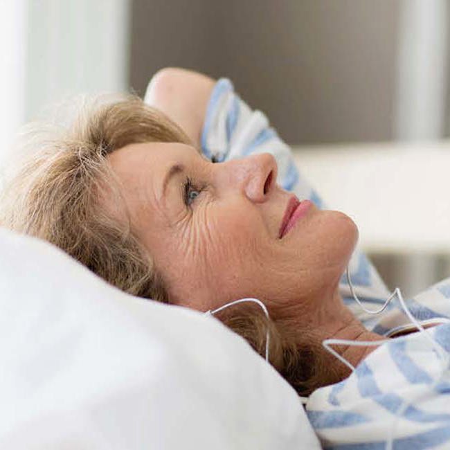 Glad kvinde ligger på ryggen i sengen med høretelefoner på.