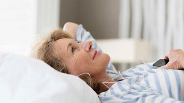 Glad kvinde ligger på ryggen i sengen med høretelefoner på.