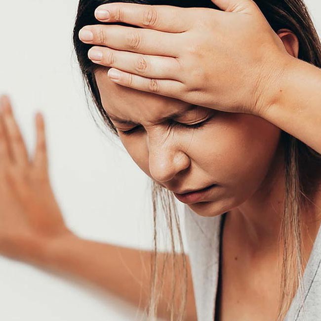 En svimmel kvinde tager sig til hovedet og støtter sig til væggen.