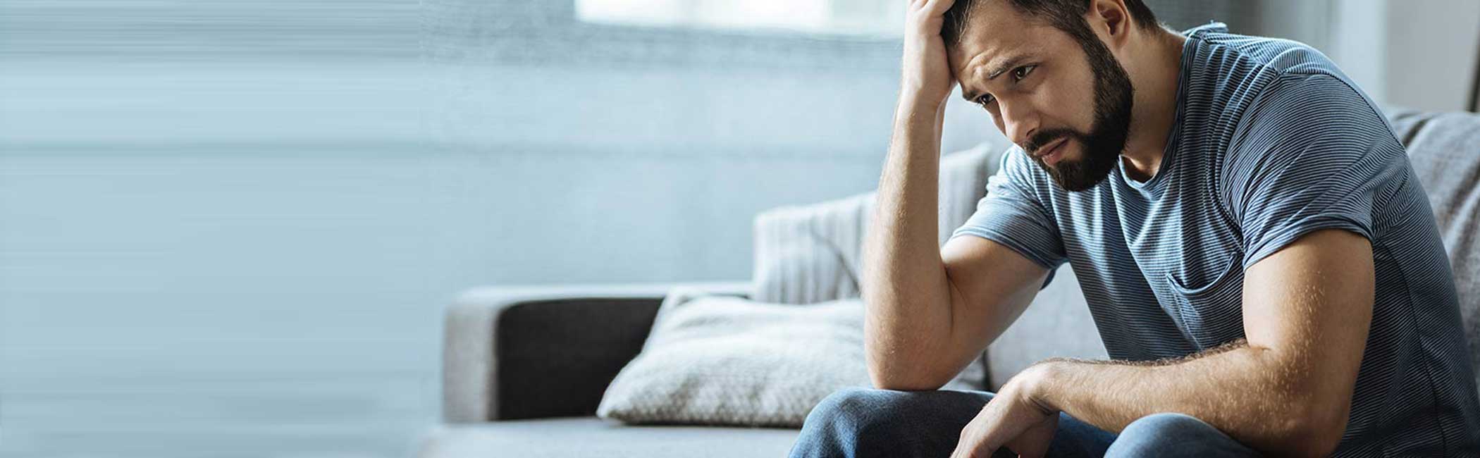 Mand sidder i sofa og ser trist ud.