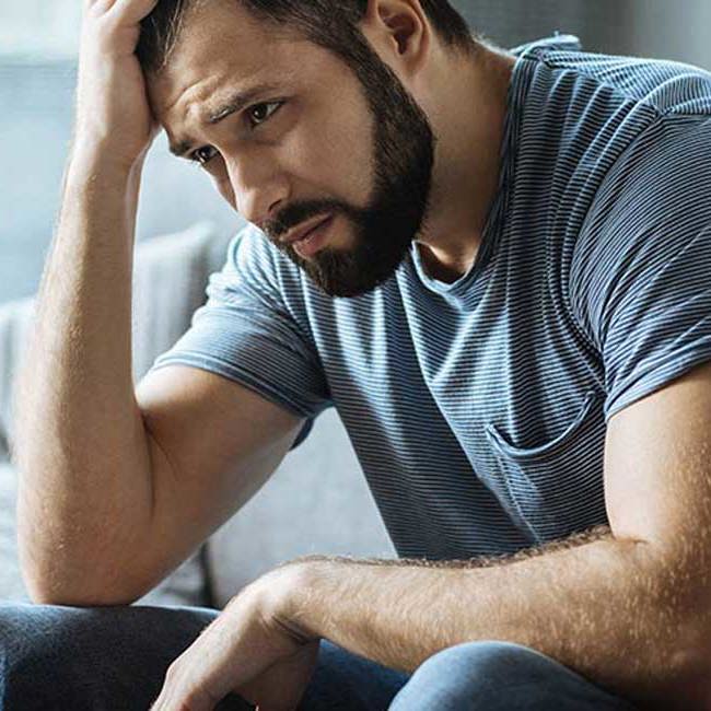 Mand sidder i sofa og ser trist ud.