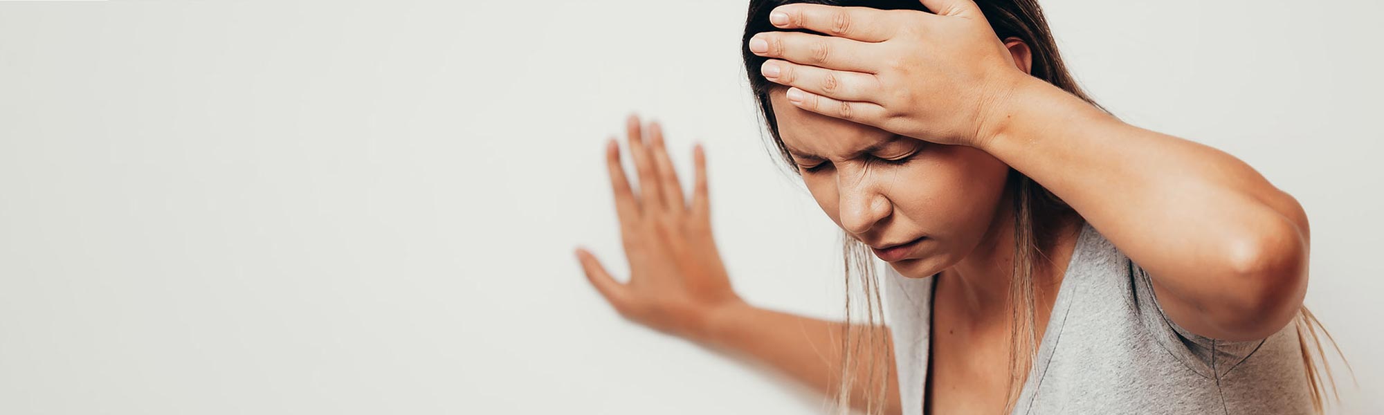 En svimmel kvinde tager sig til hovedet og støtter sig til væggen.