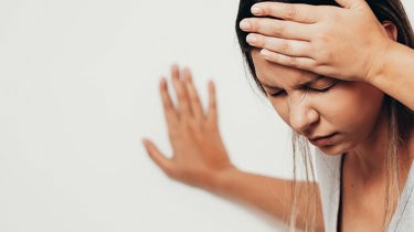 En svimmel kvinde tager sig til hovedet og støtter sig til væggen.