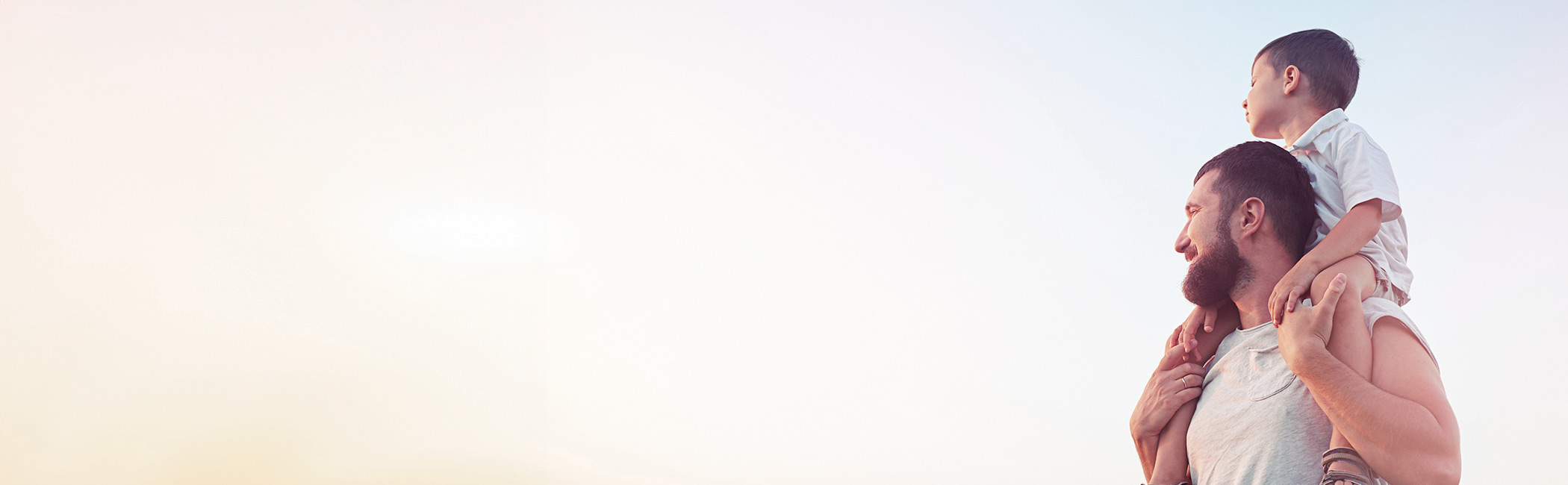 Far står med sin søn på skuldrene ude i naturen.