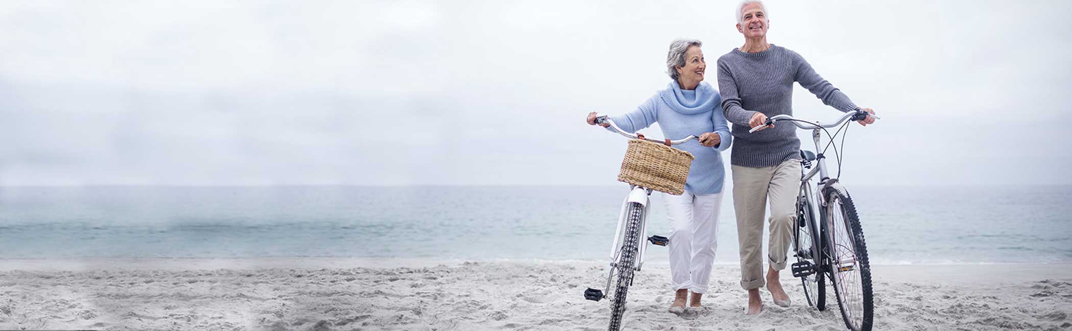 Smilende ægtepar går på stranden med deres cykler.