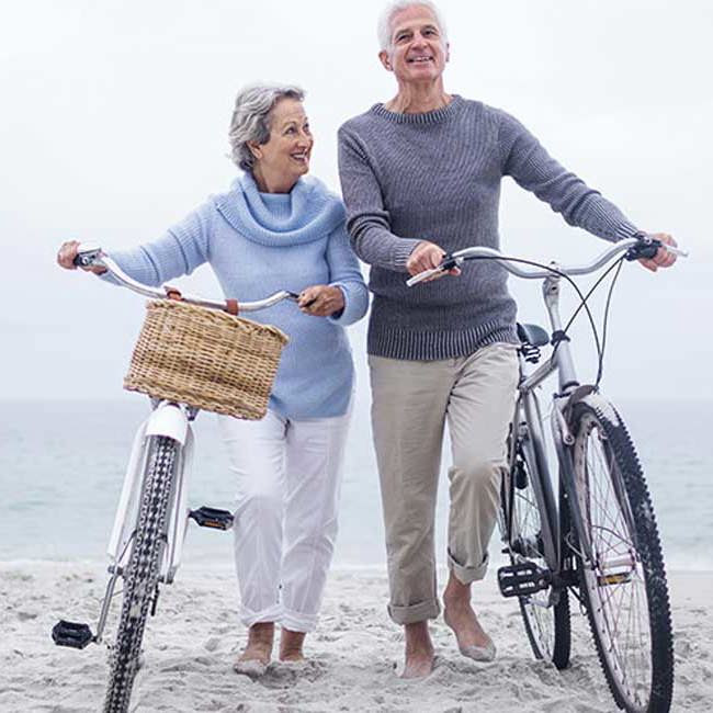 Smilende ægtepar går på stranden med deres cykler.