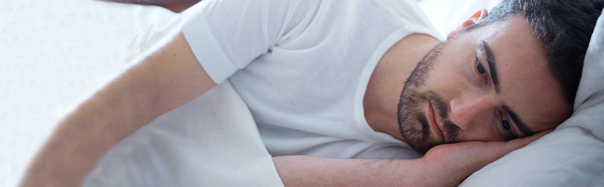 En mand ligger trist i sin seng grundet smerter fra sin blærebetændelse.