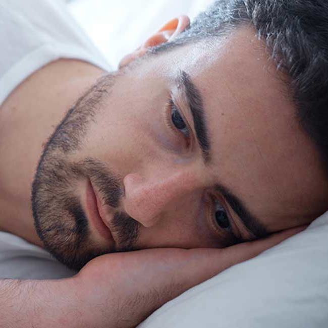 En mand ligger trist i sin seng grundet smerter fra sin blærebetændelse.